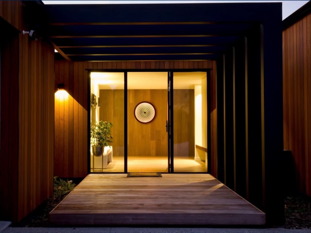 Timber-clad entryway with pergola and warm interior lighting